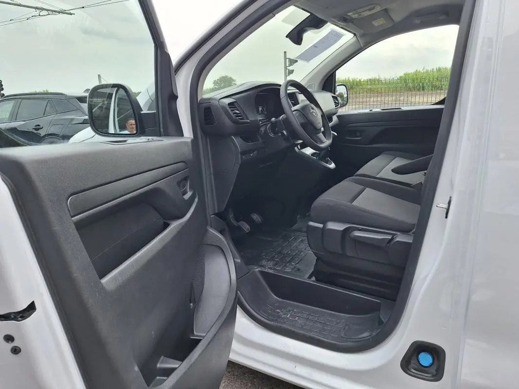 Vue intérieure côté conducteur de l'Opel Vivaro blanc 2025, montrant le tableau de bord et les sièges avant en tissu noir.