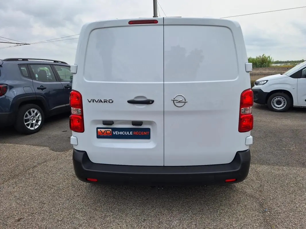 Vue arrière d'un Opel Vivaro blanc avec portes battantes et pare-chocs noir, stationné en extérieur.