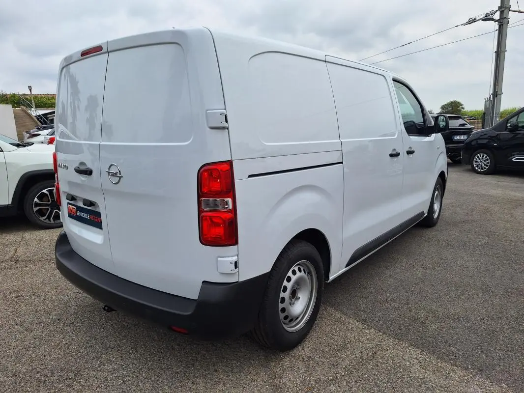 Opel Vivaro blanc vu en 3/4 arrière droit, fourgon avec porte latérale et feux arrière rouges visibles.