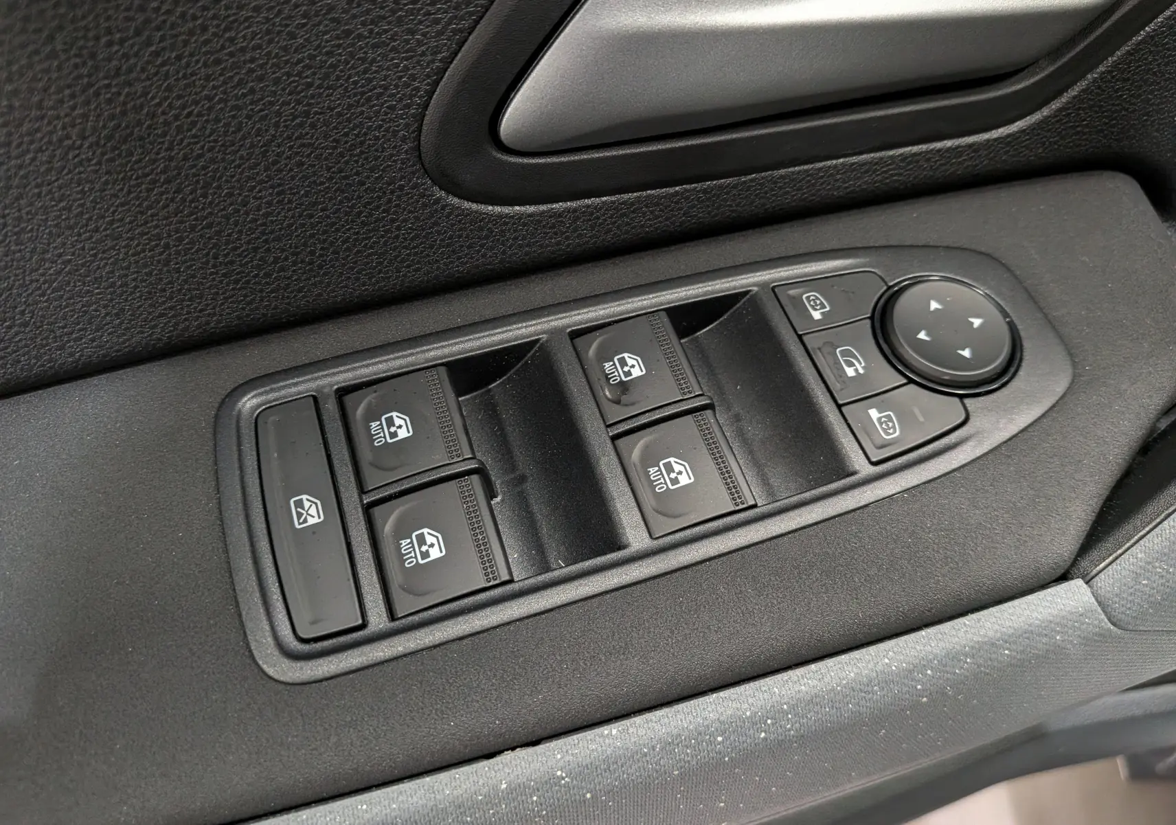 Gros plan sur les commandes de lève-vitres et rétroviseurs côté conducteur du Dacia Duster Hybrid-G blanc Glacier.