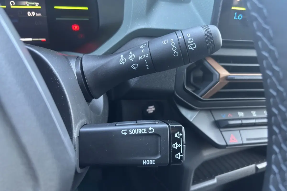 Gros plan sur les commandes au volant du Dacia Duster Hybrid-G 150, avec tableau de bord et aérateurs noirs et bronze visibles.