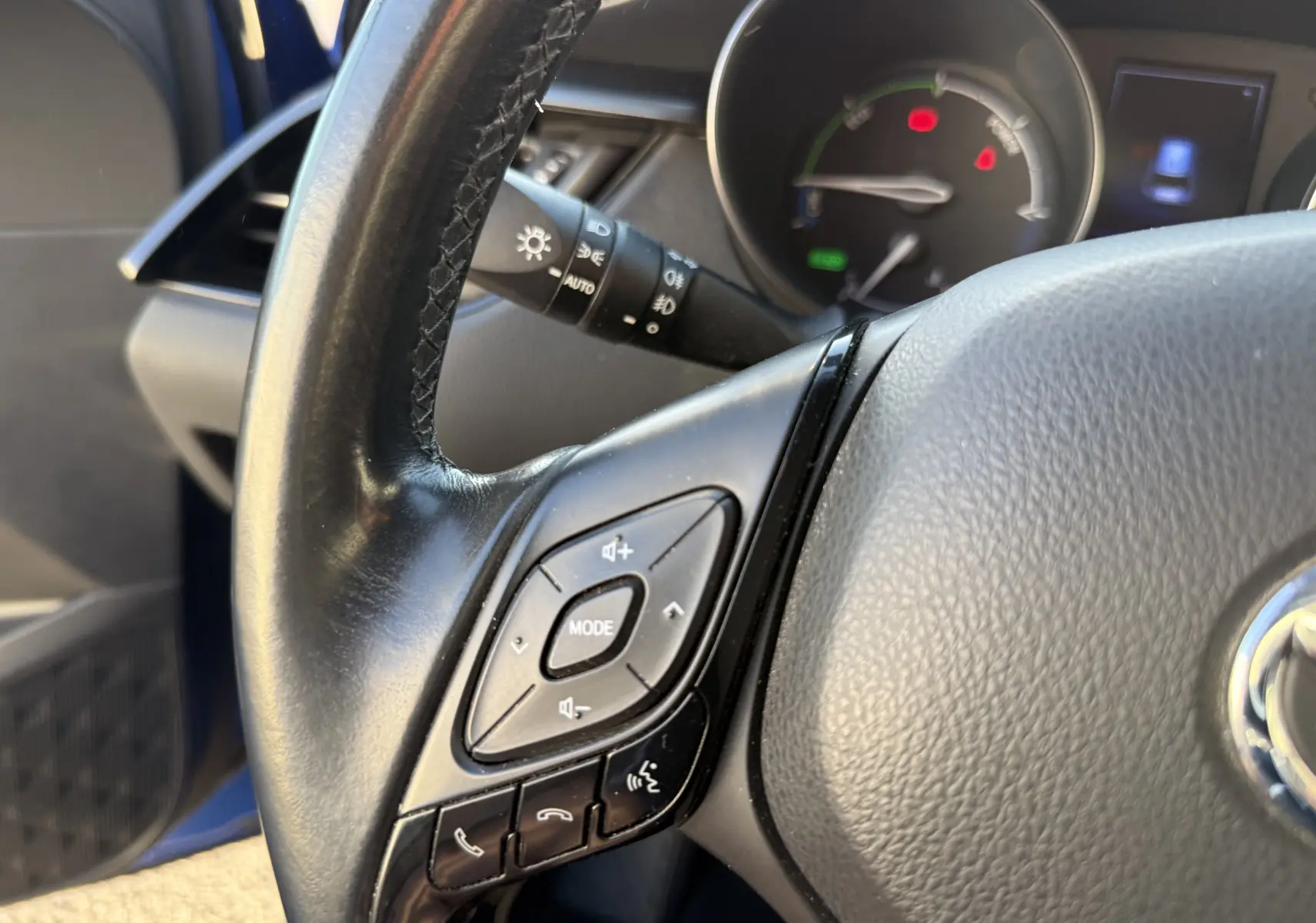 Gros plan sur le volant noir du Toyota C-HR bleu Nebula Hybrid 2018, avec commandes audio et tableau de bord partiel.