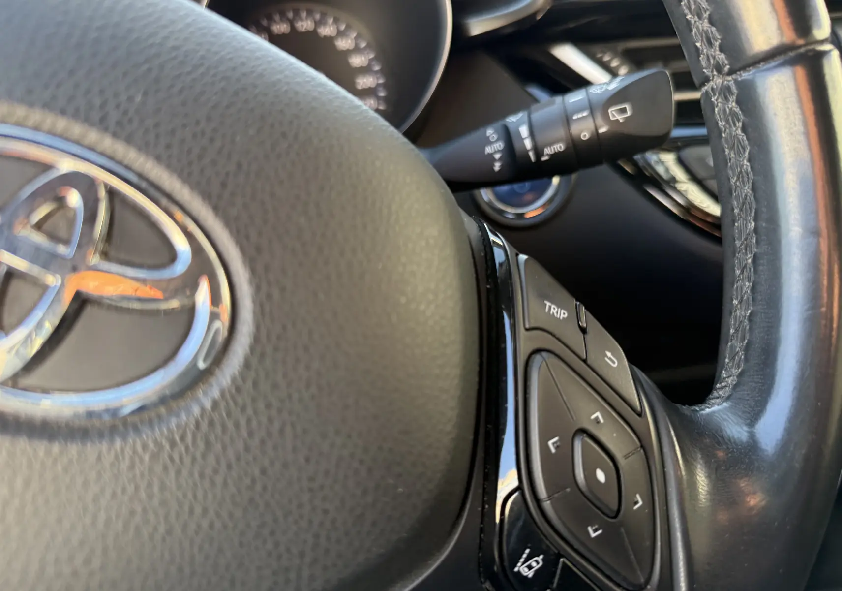 Gros plan sur le volant en cuir noir du Toyota C-HR 1.8 Hybrid 2018, avec commandes intégrées et tableau de bord flou en arrière-plan.