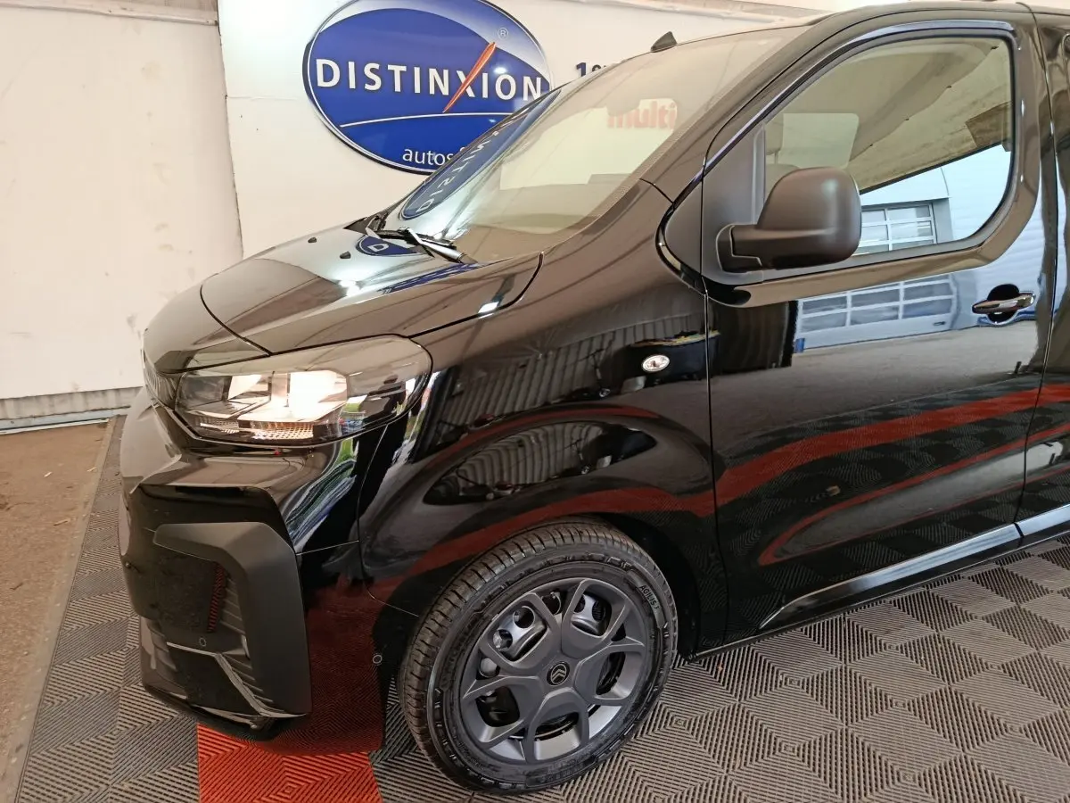 Vue 3/4 avant droit d'un Citroën Jumpy XL noir avec phares allumés et jantes spécifiques en intérieur showroom.