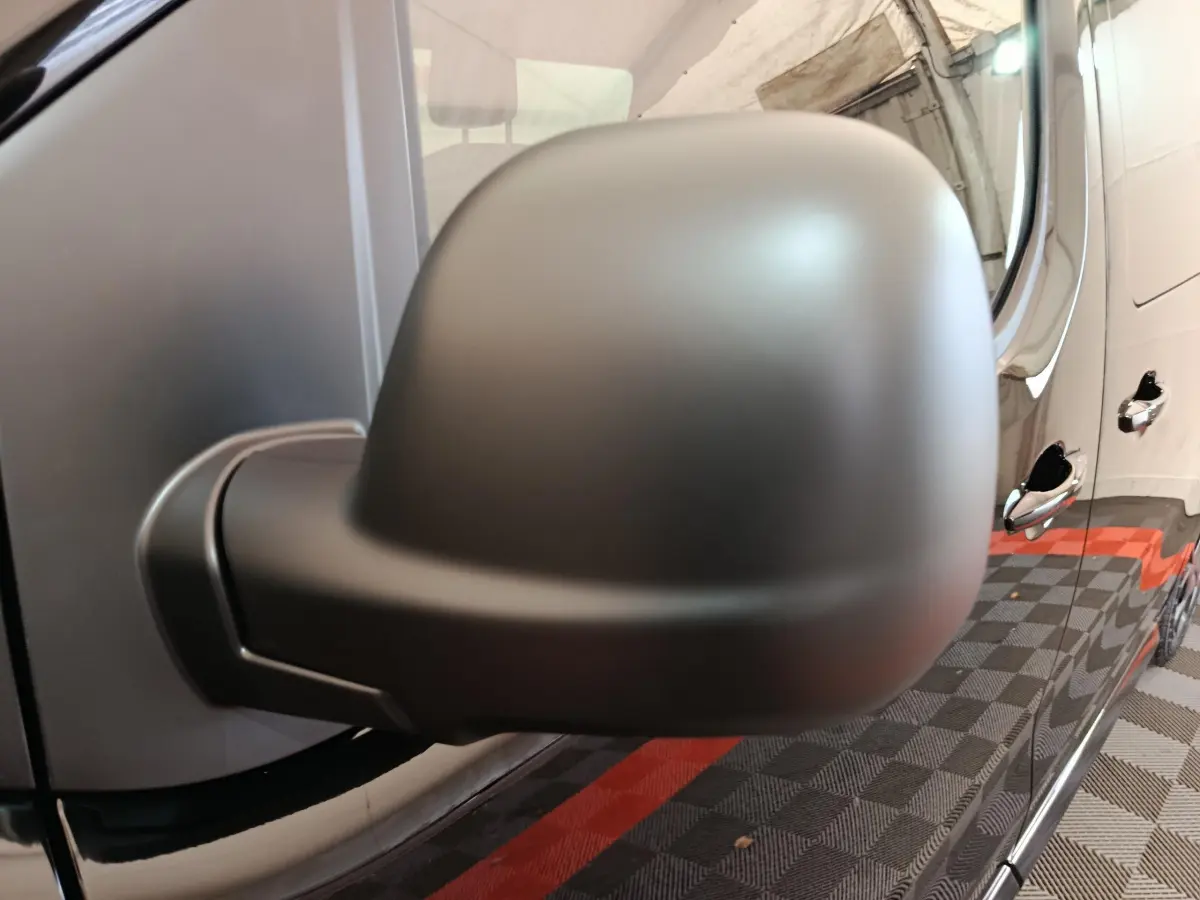Gros plan sur le rétroviseur côté conducteur du Citroën Jumpy XL noir, avec reflet des poignées de porte et sol damier rouge et noir.
