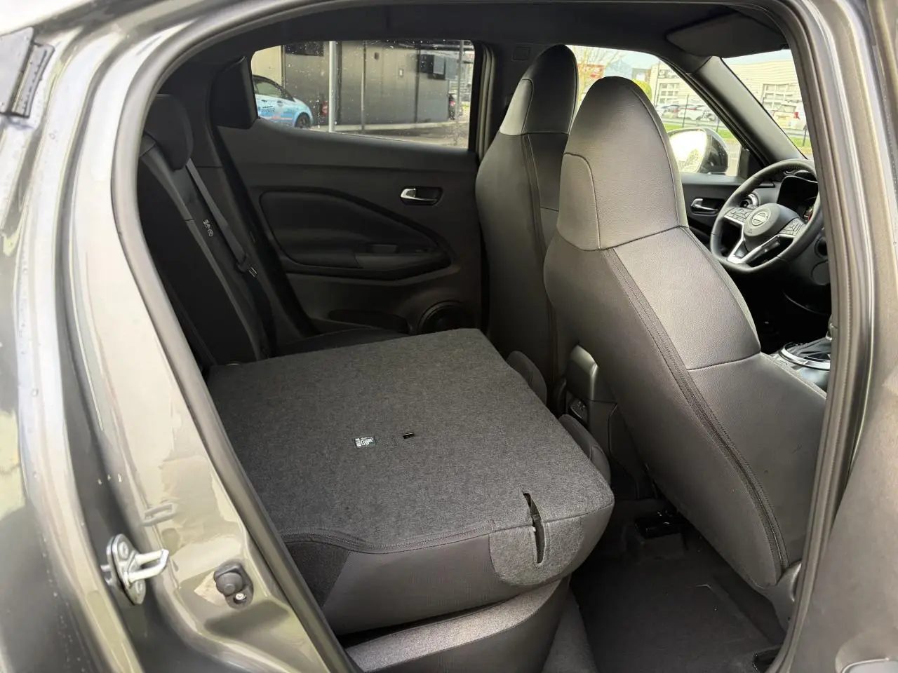 Vue intérieure côté gauche du Nissan Juke II 1.6 Hybrid 2025 noir métal avec banquette arrière rabattue.