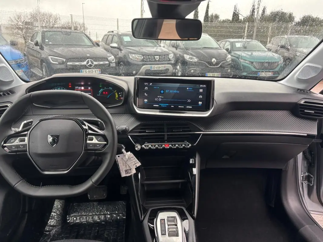 Vue intérieure avant du Peugeot 208 gris 2025, avec volant compact, écran tactile central et cockpit numérique.