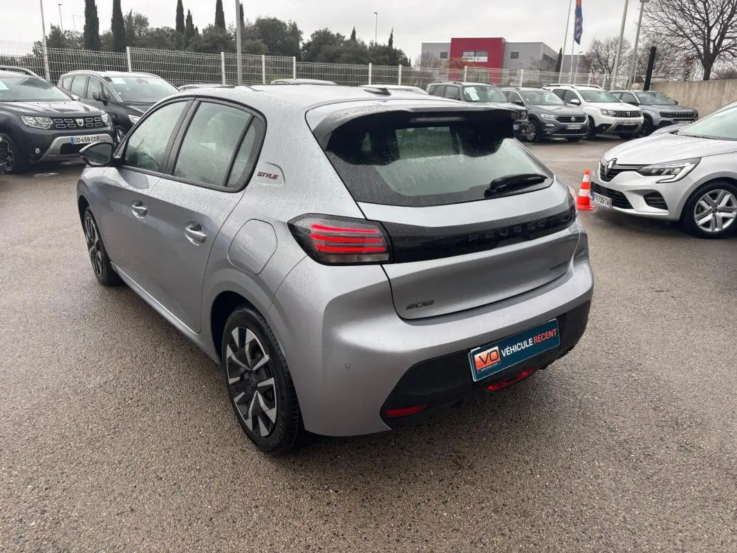 Peugeot 208 Hybrid gris vue 3/4 arrière droit, feux arrière LED et jantes 16 pouces visibles sous la pluie.