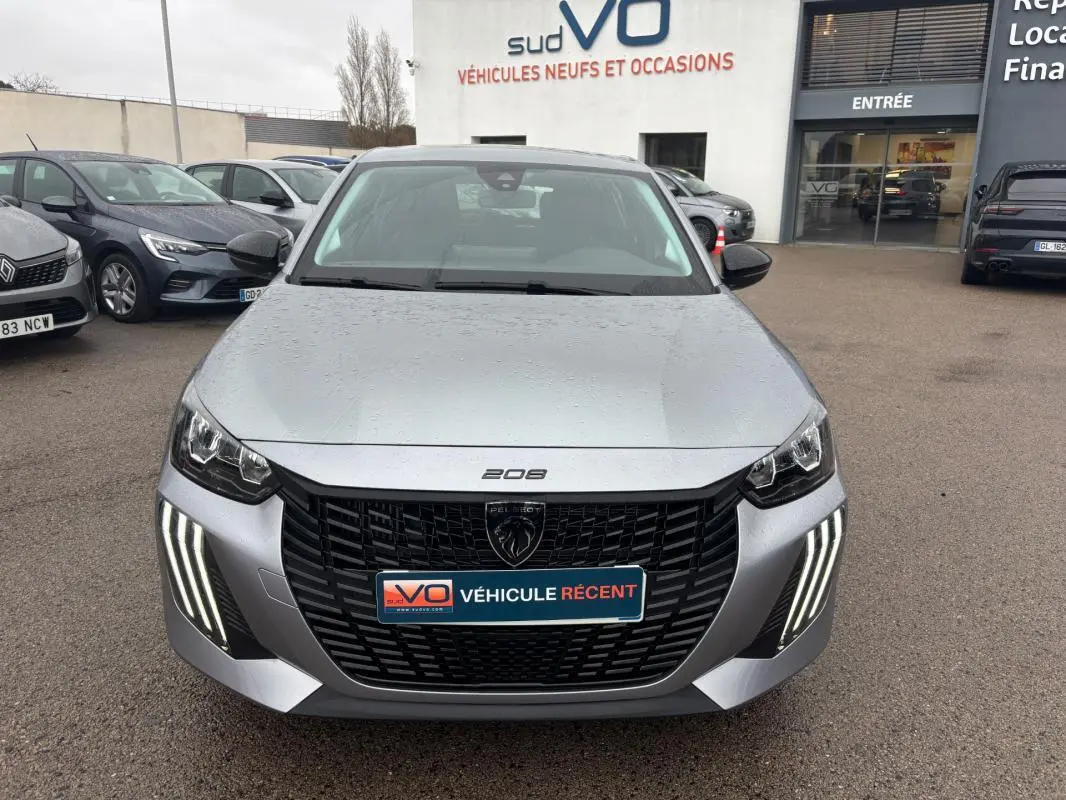 Vue avant d'une Peugeot 208 gris métallisé 2025 avec feux diurnes LED en forme de griffes et calandre noire distinctive.