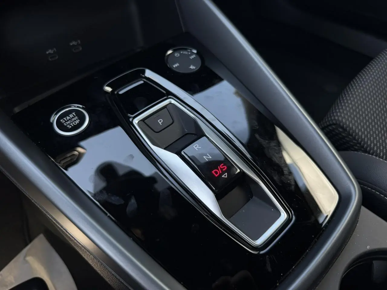Gros plan sur la console centrale noire brillante de l'Audi A3 Sportback 2025 avec levier de vitesses automatique et bouton start/stop.