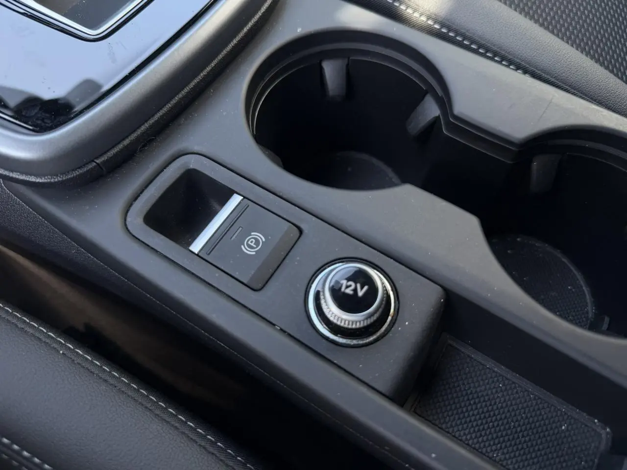 Gros plan sur la console centrale noire avec prise 12V et bouton de frein à main électrique dans une Audi A3 Sportback.
