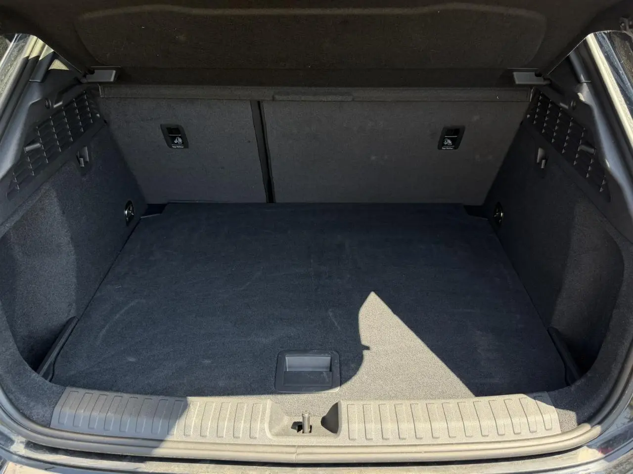 Coffre ouvert vu de l'arrière d'une Audi A3 Sportback 2025 Noir Mythe, espace de chargement vide et tapis noir.