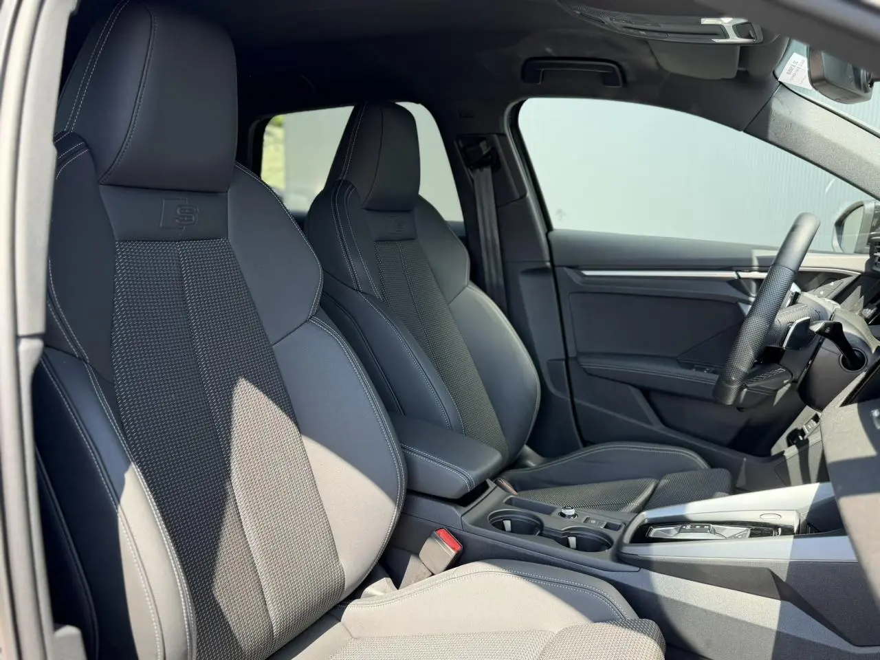 Vue intérieure côté gauche de l’Audi A3 Sportback 2025 avec sièges sport noirs et volant cuir multifonctions.