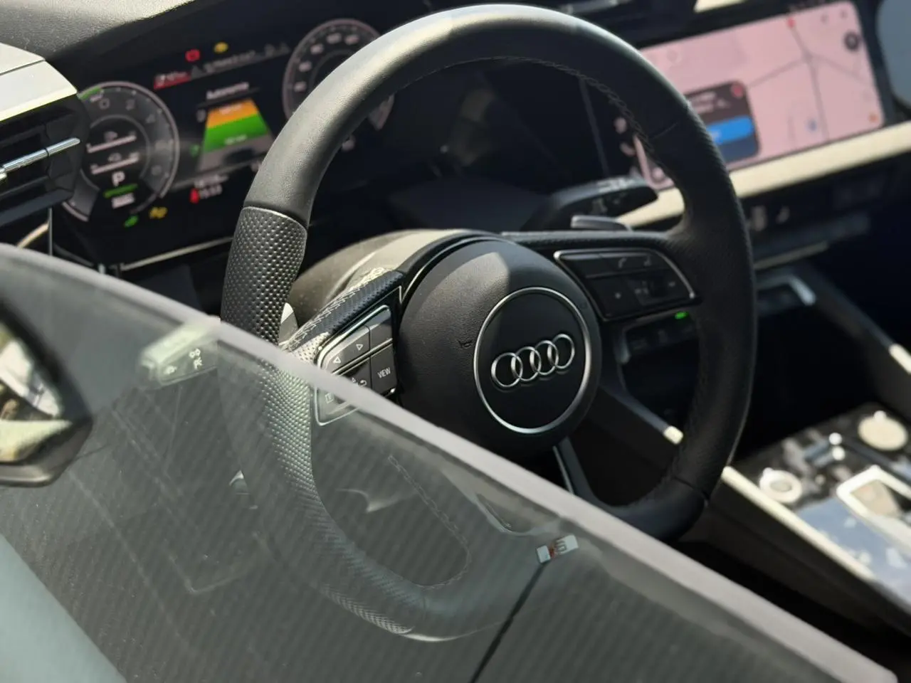 Vue intérieure centrée sur le volant cuir perforé et le tableau de bord numérique de l'Audi A3 Sportback noir Mythe.