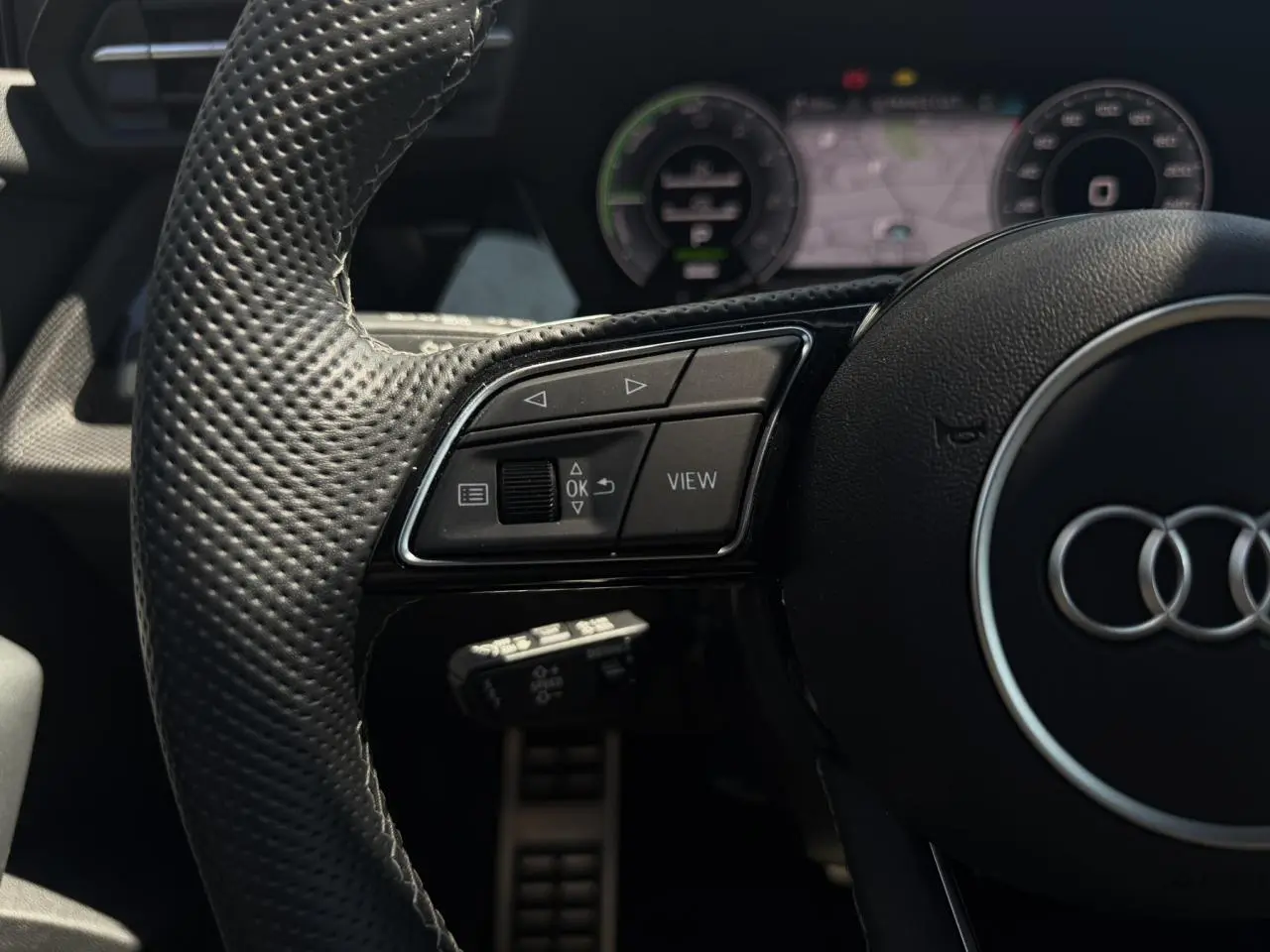 Gros plan sur le volant en cuir perforé noir de l'Audi A3 Sportback 2025 avec commandes multifonctions et tableau de bord numérique.
