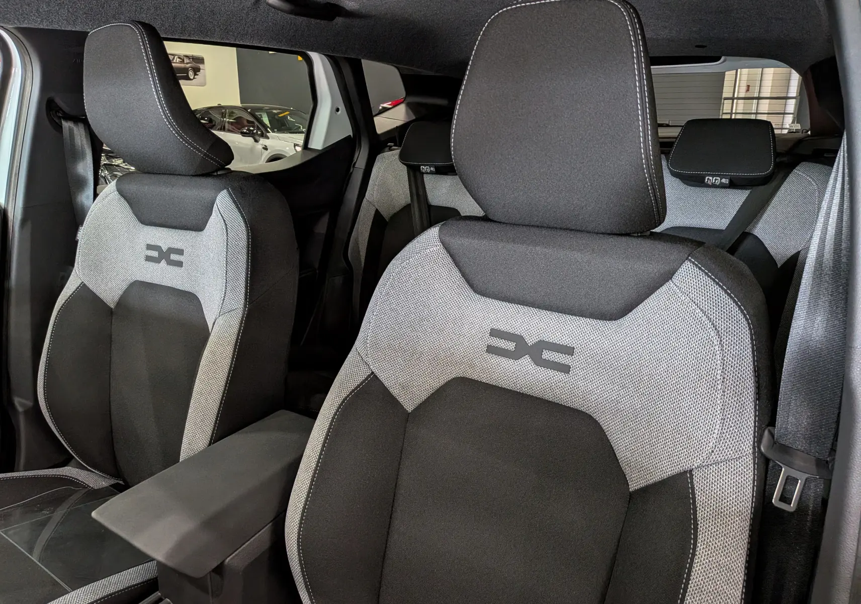 Vue intérieure rapprochée des sièges avant gris et noirs du Dacia Duster Hybrid-G 150 CH 4x4, avec logo distinctif brodé.