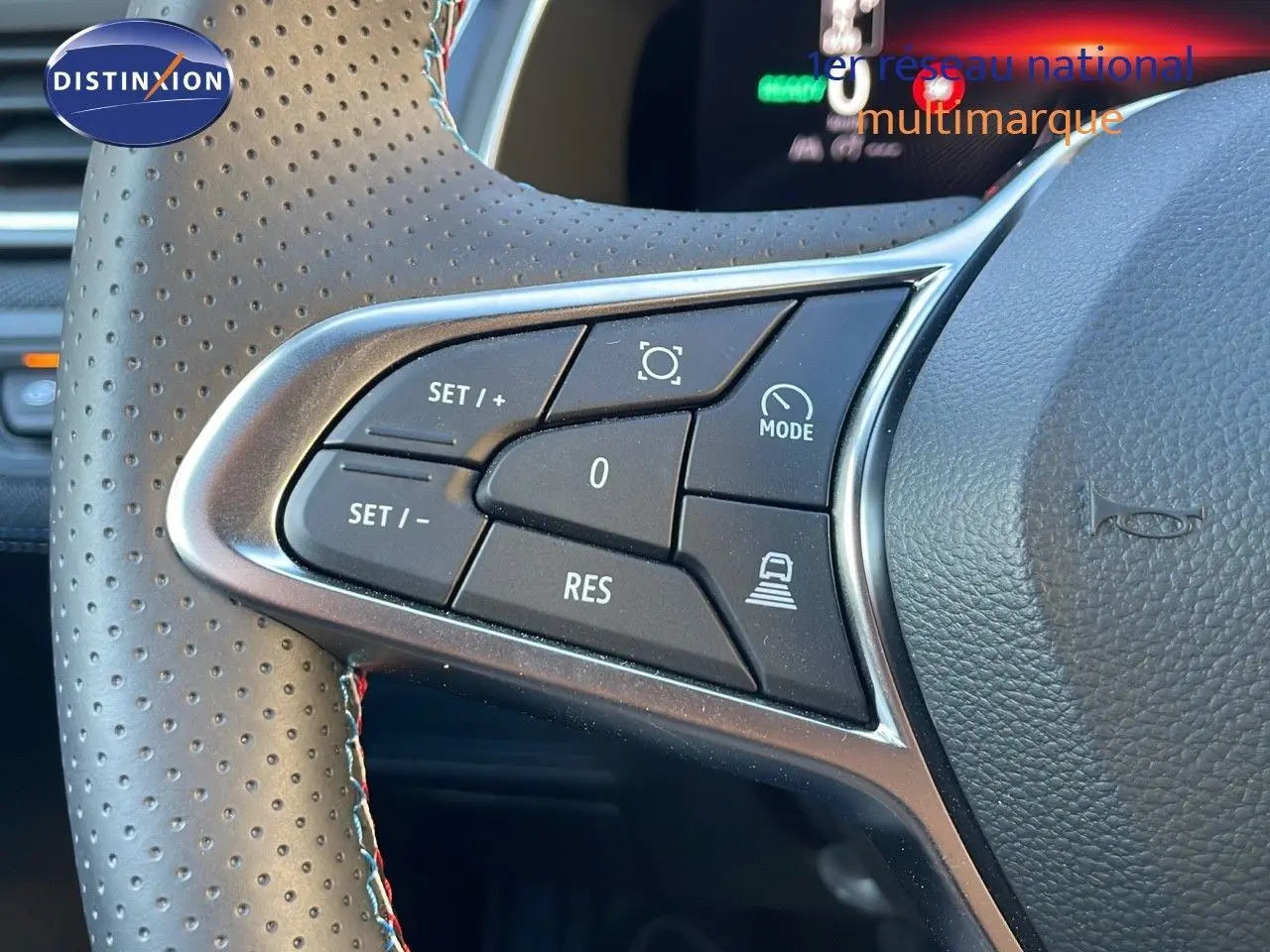 Gros plan sur les commandes de régulateur de vitesse au volant perforé d’un Renault Captur bleu Iron Metal toit noir.