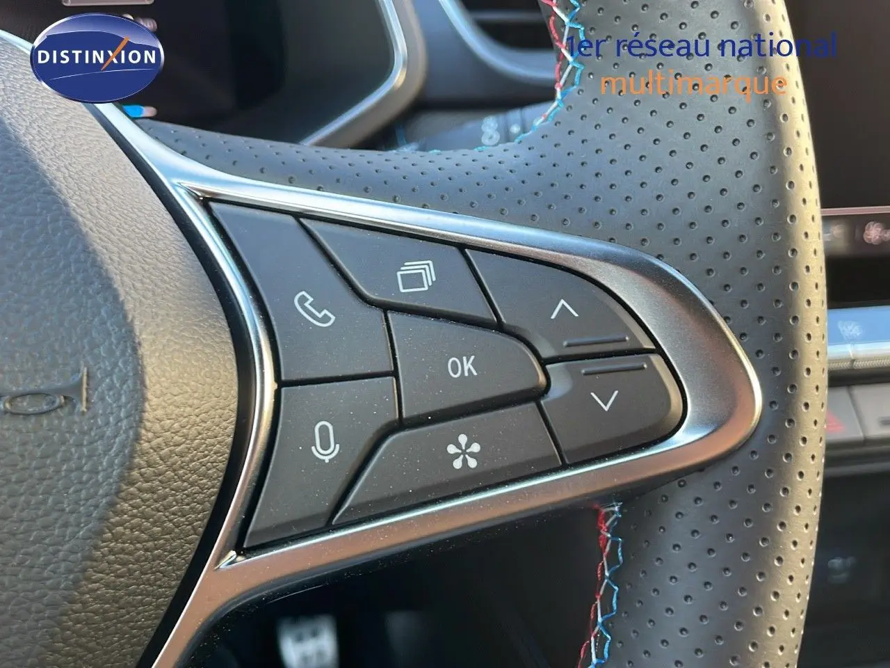 Gros plan sur les commandes au volant en cuir perforé avec surpiqûres tricolores du Renault Captur E-Tech hybride 2025.