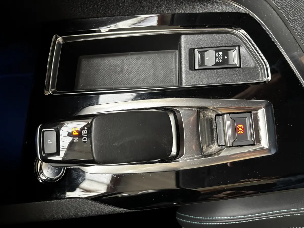 Gros plan sur la console centrale noire brillante du Peugeot 3008 hybride avec levier de vitesses et bouton frein électrique allumé.