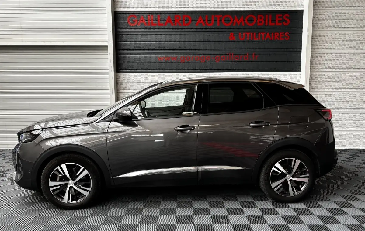 Profil côté gauche d'un Peugeot 3008 gris foncé hybride rechargeable, avec jantes alliage et vitres teintées, en intérieur showroom.