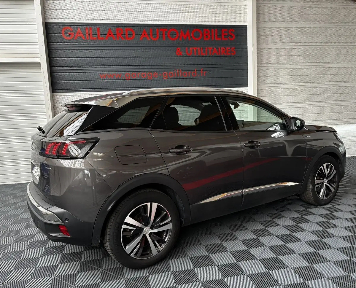 Vue 3/4 arrière droite d'un Peugeot 3008 gris foncé hybride rechargeable dans un garage avec sol damier.