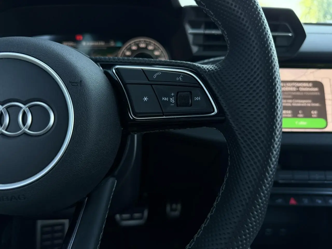 Gros plan sur le volant en cuir perforé noir de l'Audi A3 Sportback 2025 avec commandes multifonctions visibles.