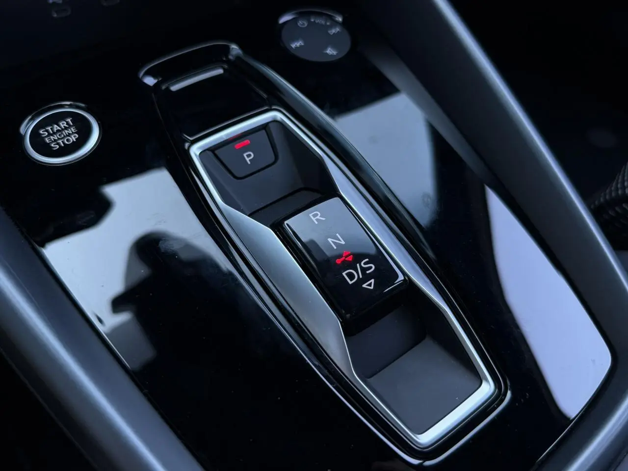 Gros plan sur la console centrale noire brillante avec sélecteur de boîte automatique et bouton Start/Stop d'une Audi A3 Sportback blanche.
