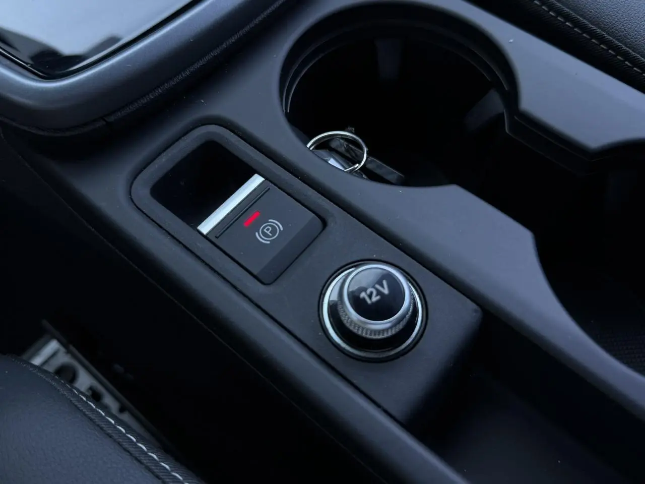 Gros plan sur la console centrale noire de l'Audi A3 Sportback 2025, avec bouton frein à main électronique et prise 12V.