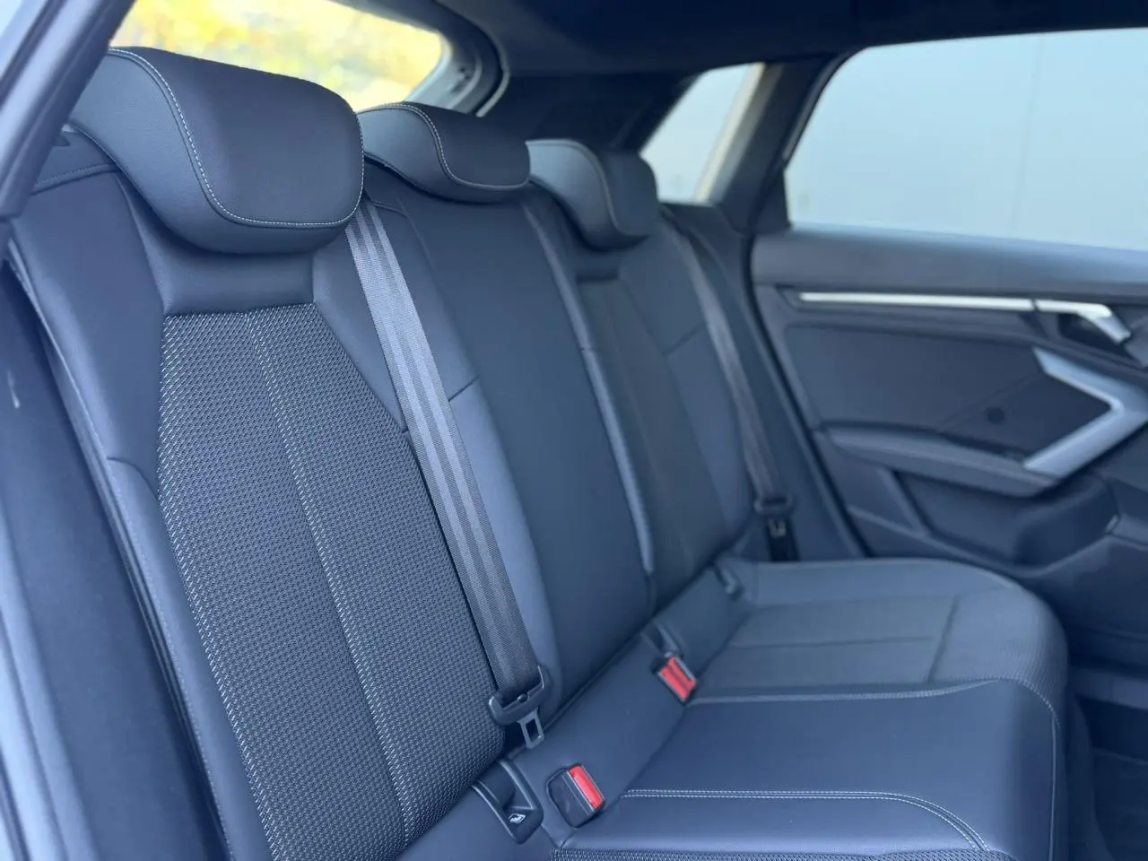 Vue intérieure des sièges arrière en tissu noir de l'Audi A3 Sportback 2025, avec ceintures de sécurité visibles.