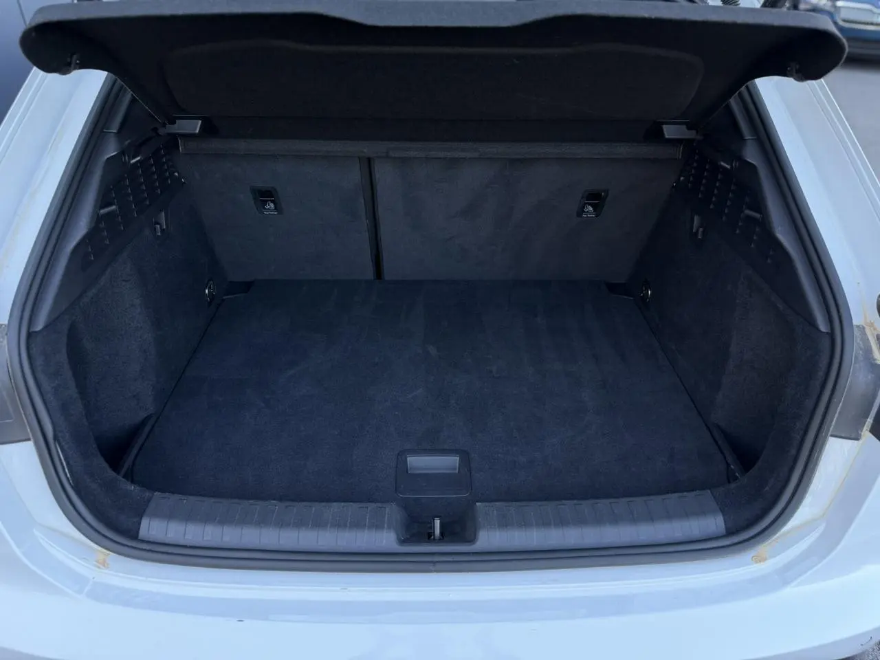 Coffre ouvert vu de l'arrière d'une Audi A3 Sportback blanc glacier, intérieur du coffre en tissu noir.