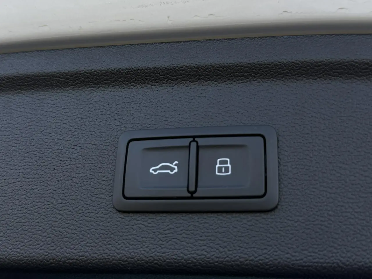 Boutons de commande pour hayon électrique et verrouillage, intégrés dans le panneau intérieur noir du coffre d'une Audi A3 Sportback blanche.