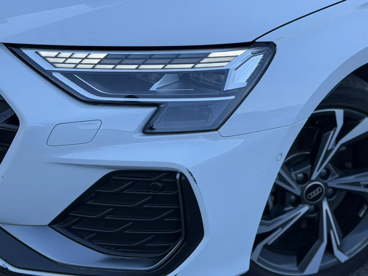 Gros plan sur l'avant droit blanc Glacier d'une Audi A3 Sportback 2025 avec phares Matrix LED et jante alliage 5 branches en Y.