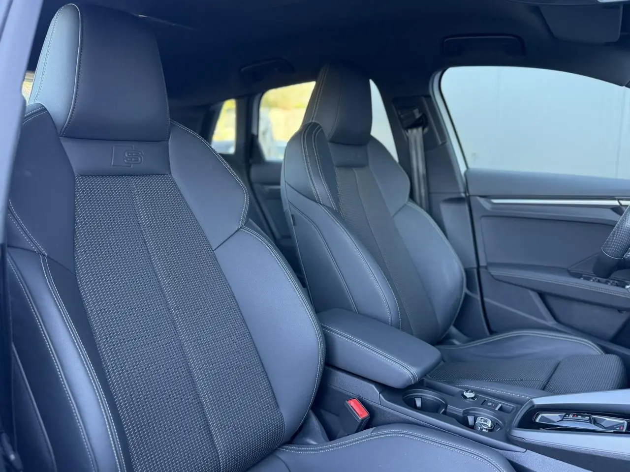 Vue intérieure côté droit des sièges sport noirs avec logo S embossé et accoudoir central coulissant de l'Audi A3 Sportback 2025.