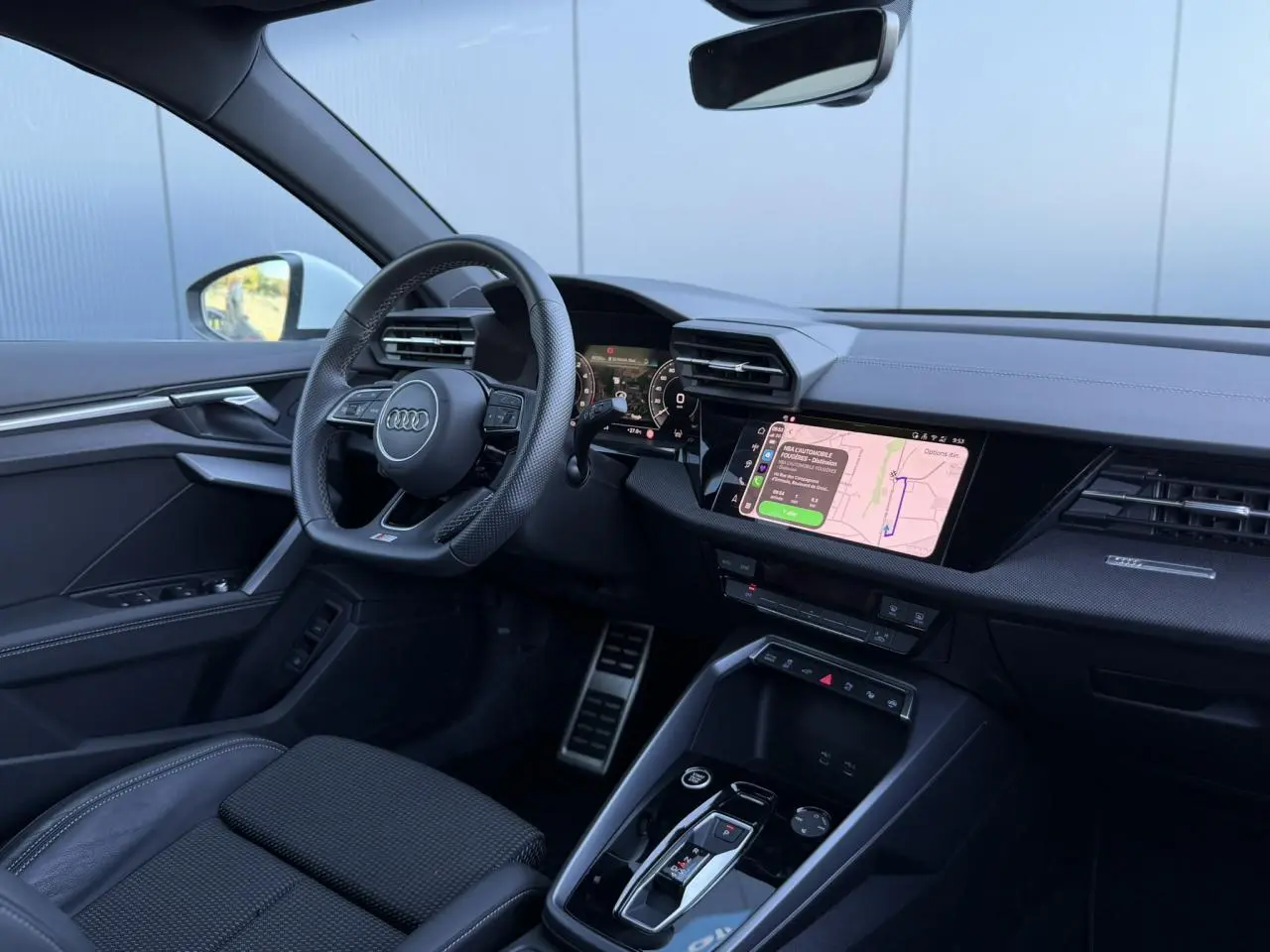 Vue intérieure côté conducteur de l'Audi A3 Sportback 2025, tableau de bord noir avec écran tactile de navigation allumé.