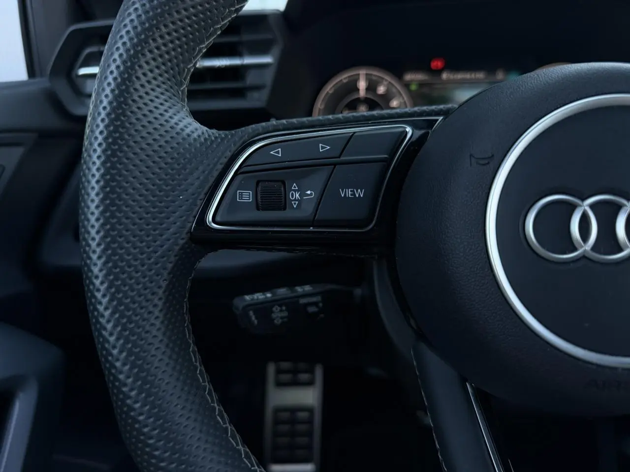 Gros plan sur le volant cuir perforé noir de l'Audi A3 Sportback 2025 avec commandes multifonctions et logo Audi central.