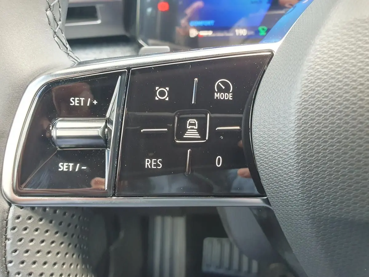 Gros plan sur les commandes au volant noir de la Renault Clio VI, avec boutons de régulateur de vitesse et mode conduite.