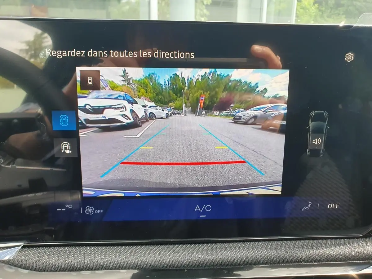 Écran multimédia de Renault Clio VI montrant la caméra de recul avec vue arrière dégagée sur parking extérieur.