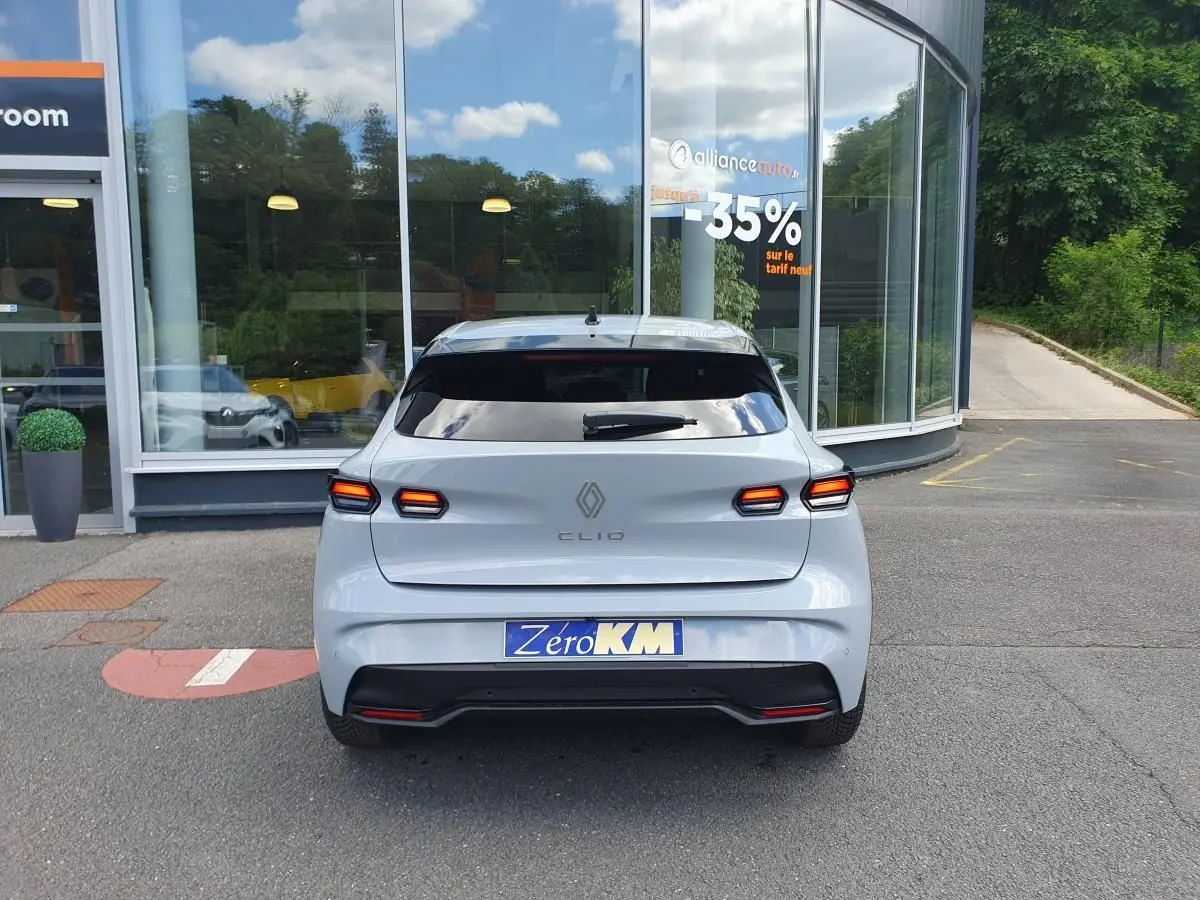 Vue arrière d'une Renault Clio VI gris Rafale avec feux LED et lunette arrière surteintée, stationnée devant une vitrine.