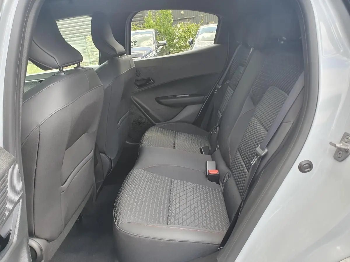 Vue intérieure arrière côté droit de la Renault Clio VI gris Rafale, montrant les sièges arrière en tissu et cuir avec surpiqûres rouges.