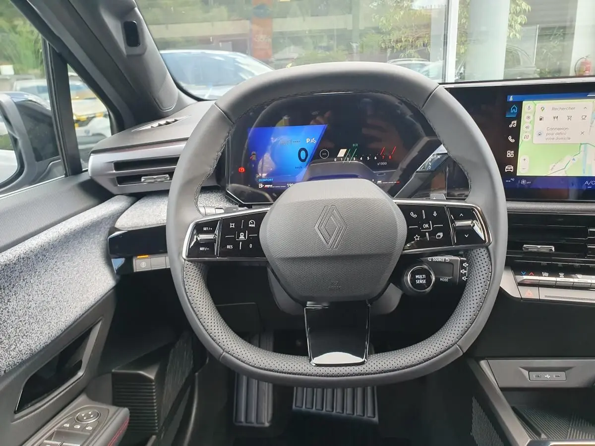 Vue intérieure centrée sur le volant multifonction de la Renault Clio VI avec tableau de bord numérique et écran tactile.