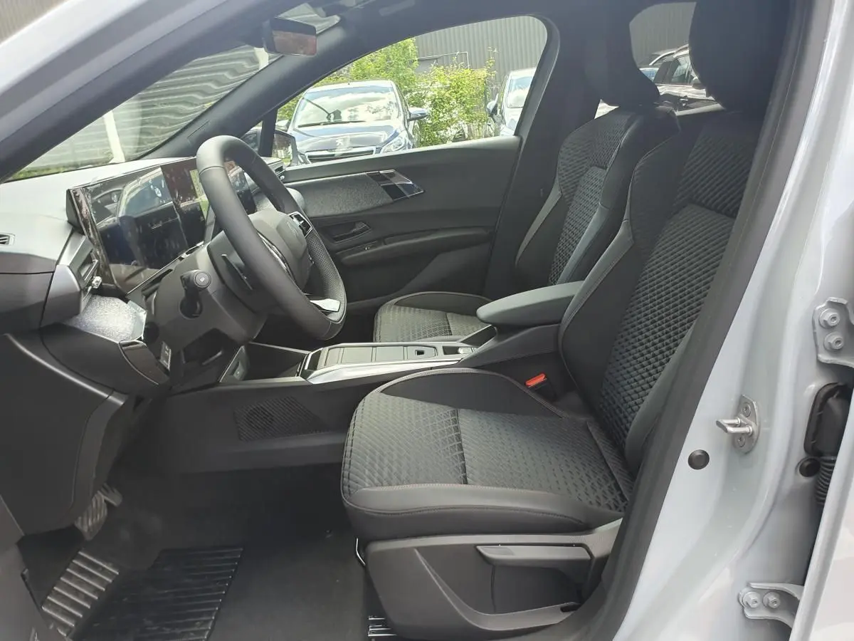 Vue intérieure côté conducteur de la Renault Clio VI avec sièges tissu noir et tableau de bord moderne.