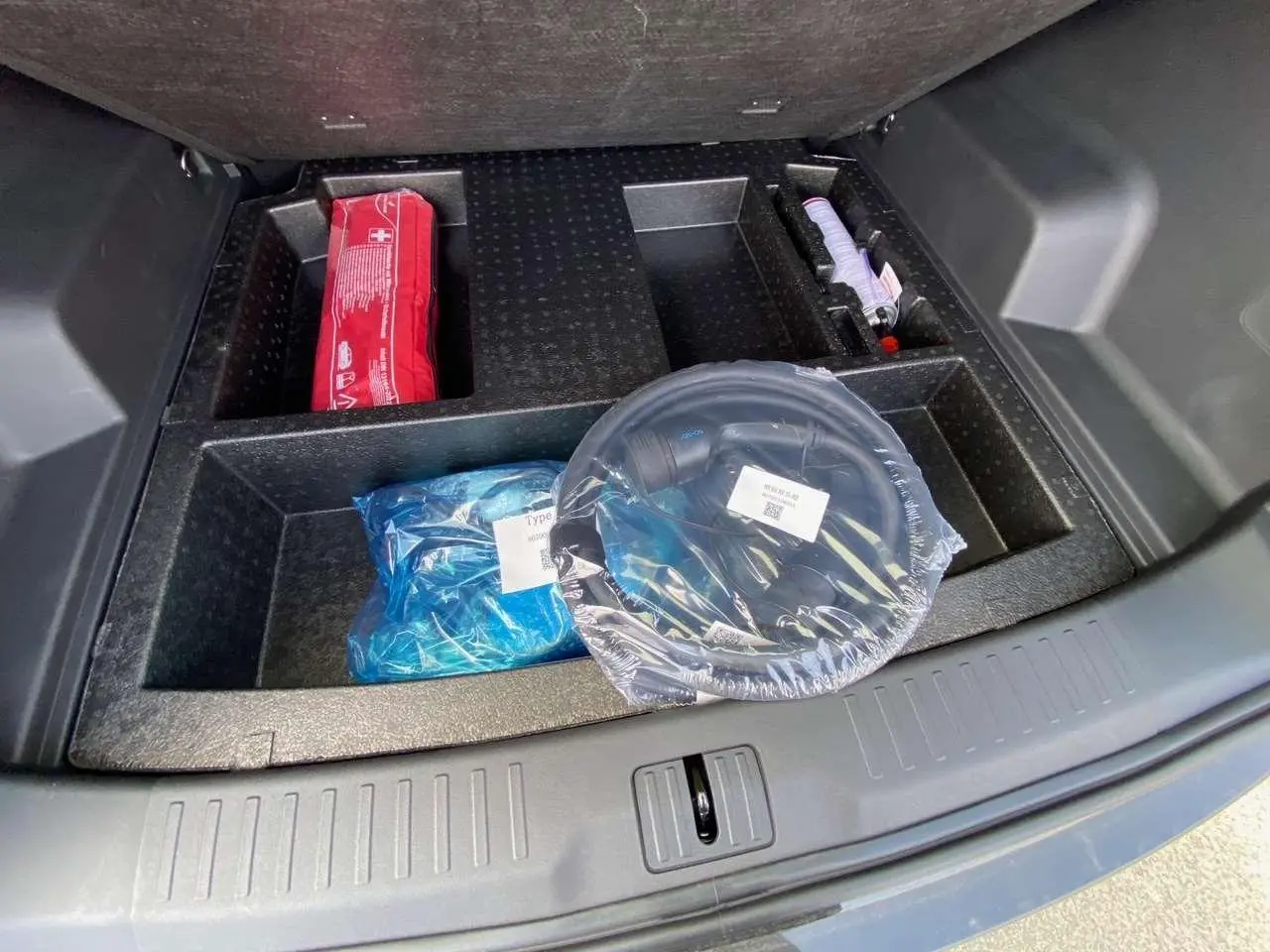 Coffre ouvert du JAECOO J7 1.5 PHEV Selective 2026, vue plongeante sur rangement avec accessoires emballés.