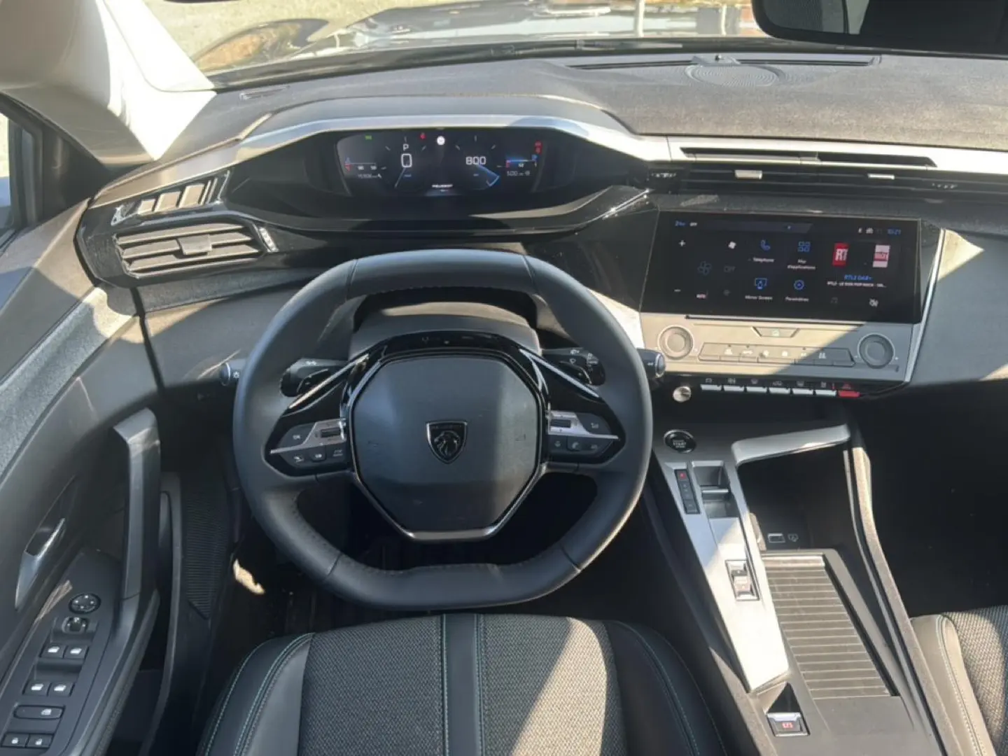 Vue intérieure du poste de conduite de la Peugeot 308 2025, volant multifonction et écran tactile central visibles.