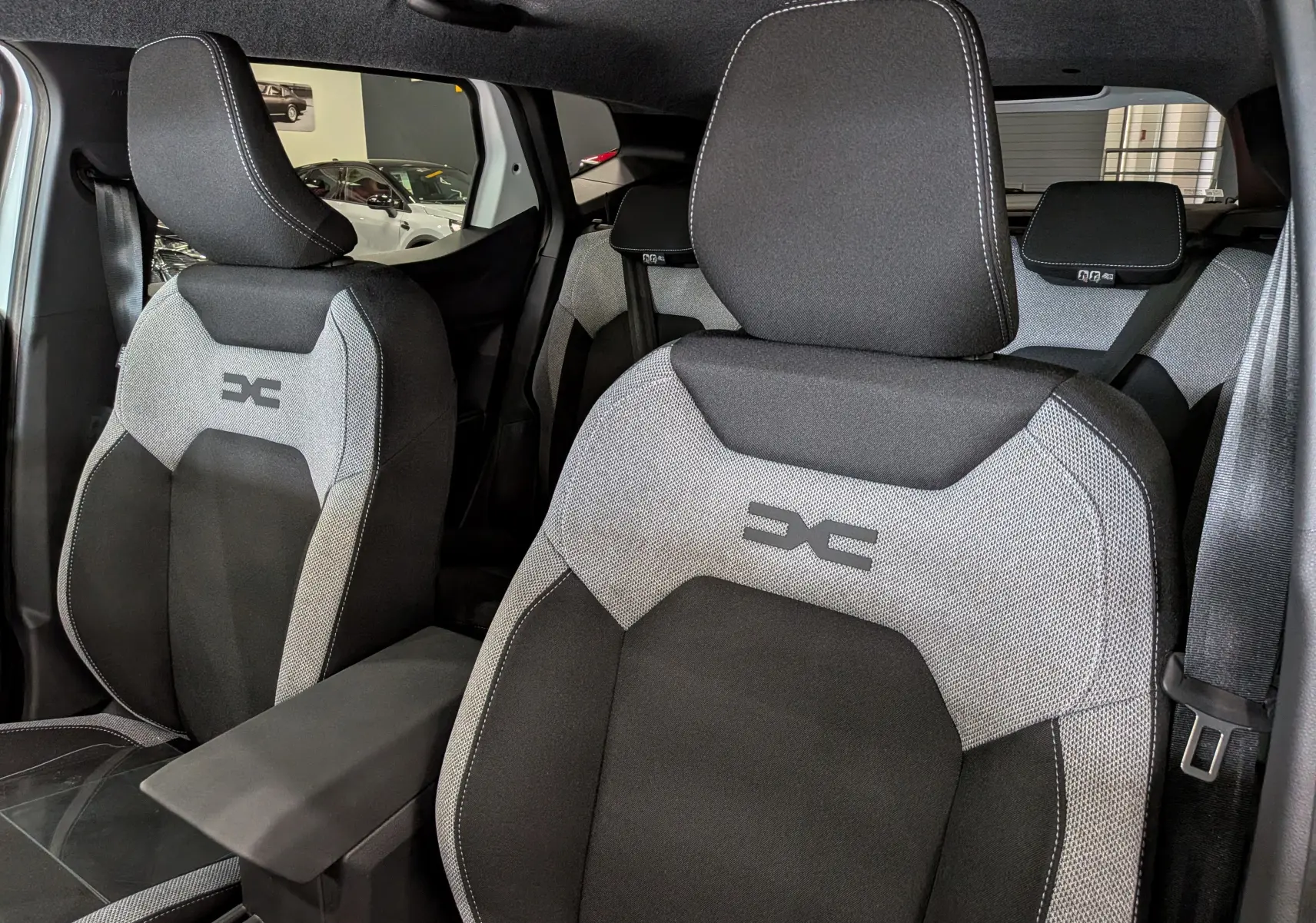 Vue intérieure rapprochée des sièges avant gris et noirs du Dacia Duster Hybrid-G 150 CH 4x4 Journey avec logo distinctif brodé.