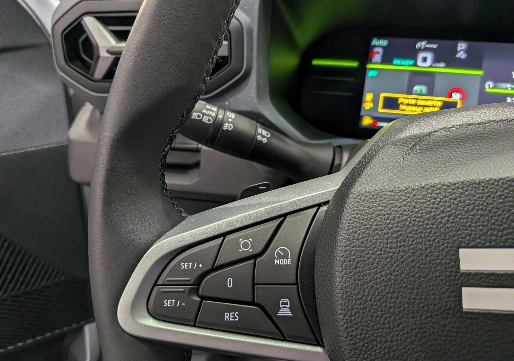 Gros plan sur le volant côté gauche du Dacia Duster Hybrid-G 150 CH 4x4 blanc, avec commandes multifonctions et tableau de bord numérique.