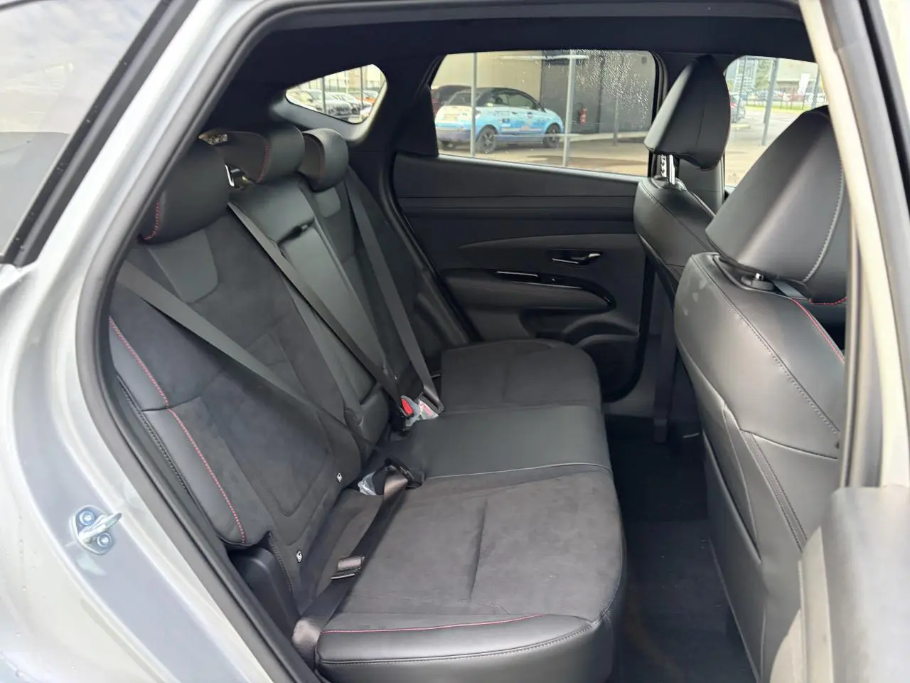 Vue intérieure côté gauche des sièges arrière cuir/alcantara noirs avec surpiqûres rouges du Hyundai Tucson 2025 Shimmering Silver.