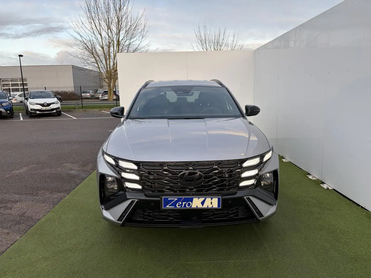 Vue avant d'un Hyundai Tucson 2025 gris argent métallisé avec calandre noire N Line et feux LED allumés.