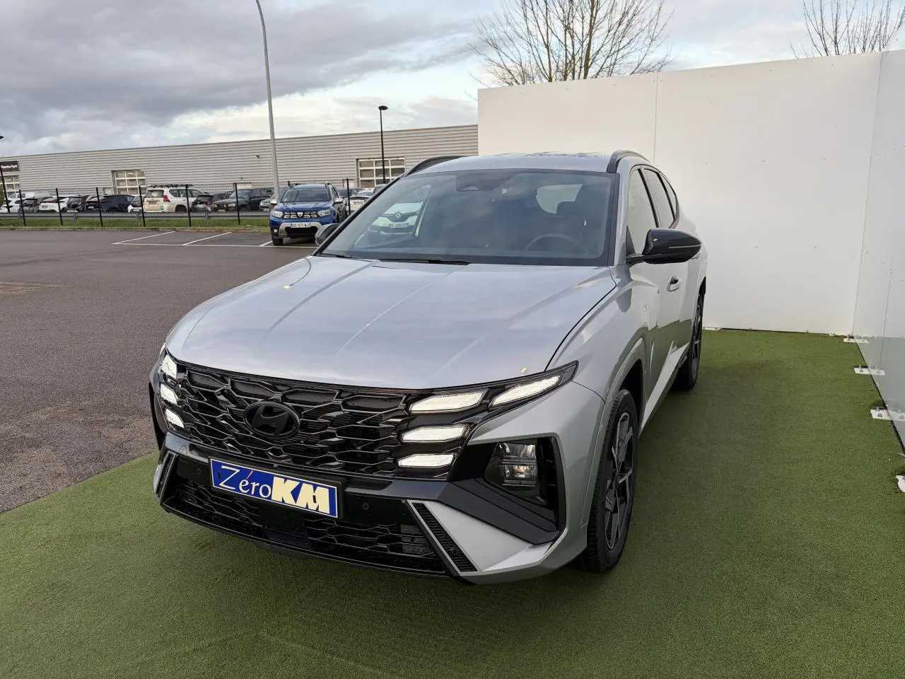 Vue 3/4 avant d'un Hyundai Tucson 2025 gris argent métallisé avec calandre noire et jantes alliage sombres.