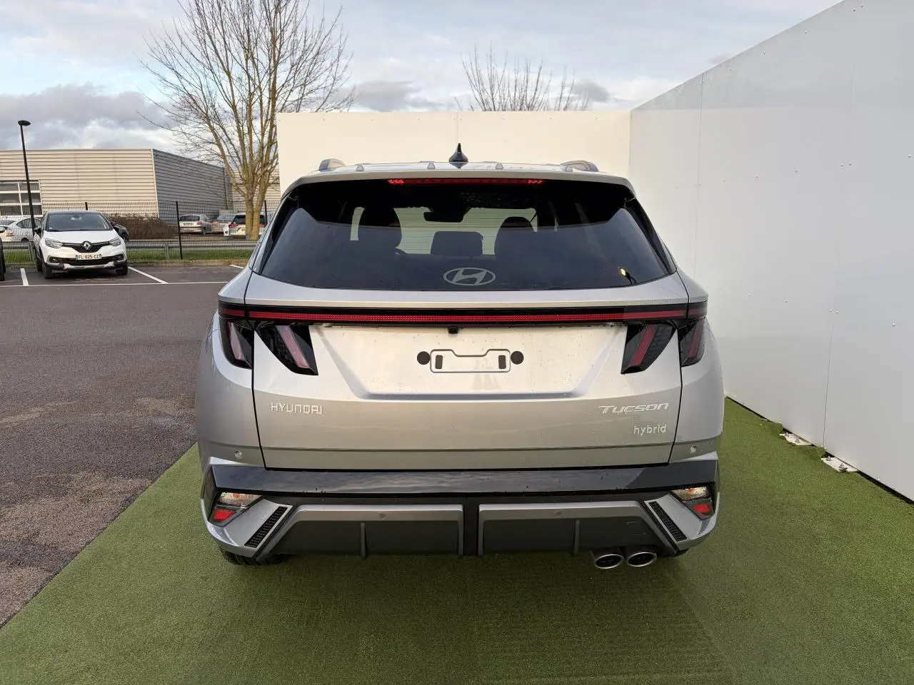 Vue arrière d'un Hyundai Tucson 2025 hybride en argent métallisé avec feux arrière LED et double sortie d'échappement côté droit.