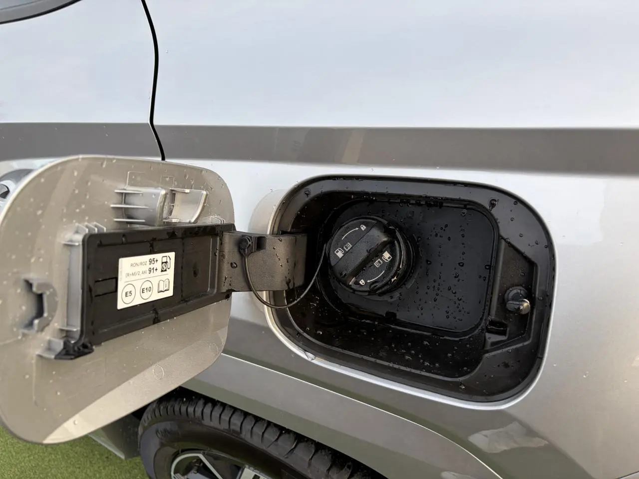 Trappe de carburant ouverte côté gauche d’un Hyundai Tucson 2025 gris argent métallisé avec bouchon noir et gouttes d’eau.